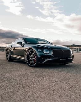 Sleek black Bentley Continental GT in a low-angle shot with a scenic sky in the background
