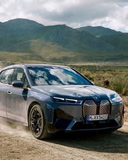 BMW iX driving on a dirt road with mountains in the background, featured on a watch face