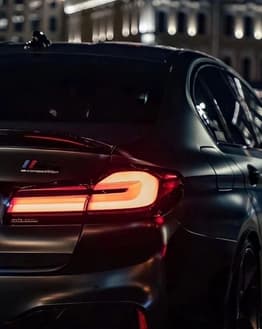 BMW M5 Competition rear view at night with illuminated taillights and city lights in the background, featured on a watch face