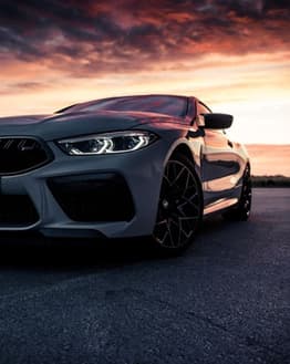 Front view of a BMW M8 with a vibrant sunset in the background, featured on a watch face