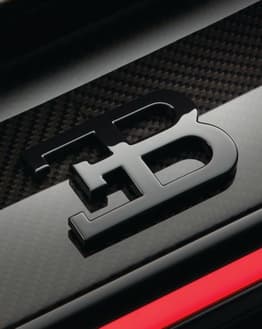 Close-up of the Bugatti EB logo in glossy black on a carbon fiber background with a red accent, featured on a watch face.
