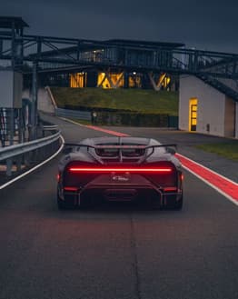 Rear view of a Bugatti Chiron with a red taillight on a racetrack during dusk, featured on a watch face.