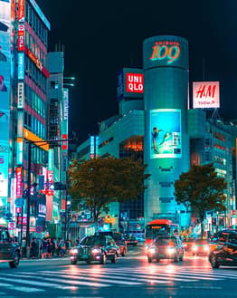 Nighttime view of Shibuya's bustling streets with neon lights, cars, and the iconic Shibuya 109 building, displayed on a watch face