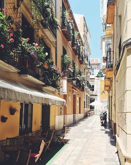 Sunlit Mediterranean alley with vibrant flowers on balconies and cozy outdoor cafes, displayed on a watch face