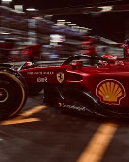 Close-up of a Ferrari F1 car speeding through the pit lane at night, with a blurred background of lights, featured on a watch face.