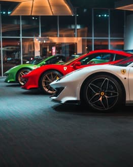 A lineup of Ferrari supercars in white, red, and green, displayed in a luxurious showroom, featured on a watch face.
