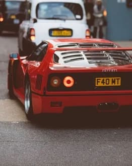 Rear view of a red Ferrari F40 driving through city streets, showcasing its iconic taillights and bold design, featured on a watch face.