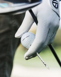 A watch face featuring a gloved hand holding a golf ball and tee, showcasing the essence of the game.