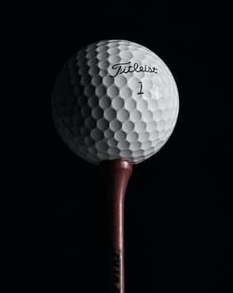 A watch face featuring a close-up of a Titleist golf ball on a tee with a dark background.