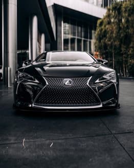 Front view of a black Lexus car parked in an urban setting, featured on a watch face.