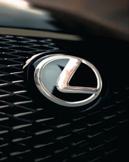 Close-up of the Lexus logo on a textured grill background, featured on a watch face.