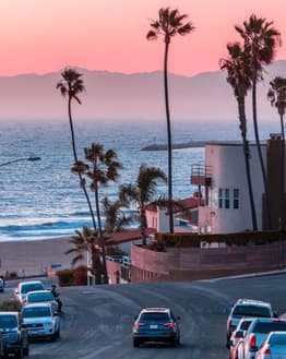 A coastal neighborhood overlooking the ocean with palm trees and a vibrant sunset sky, designed for a watch face.