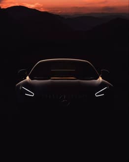 Silhouette of a Mercedes car with glowing headlights, set against a dramatic mountain sunset, featured on a watch face.