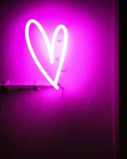 Glowing pink neon heart on a textured wall, featured on a watch face.