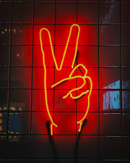 Neon peace sign in yellow on a red tiled background, designed for a watch face.