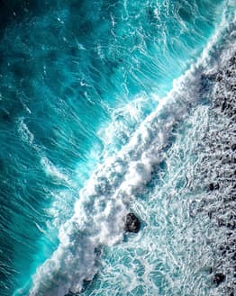 Aerial view of turquoise ocean waves crashing onto a rocky shoreline, designed for a watch face.
