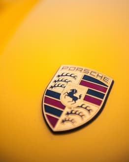 Close-up of the Porsche emblem on a vibrant yellow surface, featured on a watch face.