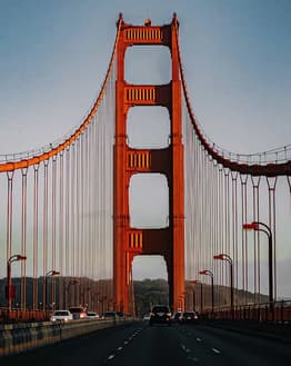 Photograph of the Golden Gate Bridge in San Francisco, showing its red suspension structure and scenic roadway during sunset, featured on a watch face.