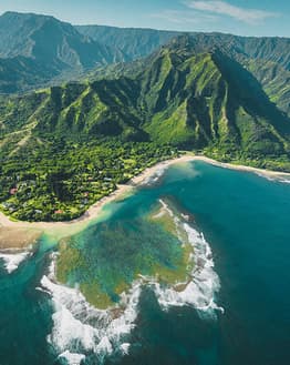Aerial photograph of a tropical island with lush green mountains, crystal-clear turquoise waters, and coral reefs, creating a breathtaking coastal scene, featured on a watch face.
