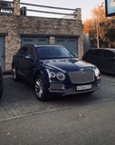 Front view of a blue Bentley Bentayga SUV parked in front of a rustic brick building