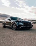 Sleek black Bentley Continental GT in a low-angle shot with a scenic sky in the background