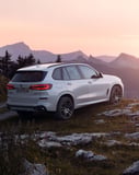 White BMW X5 parked on rocky terrain with a sunset mountain backdrop on a watch face