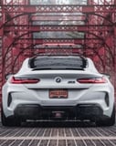Rear view of a white BMW M8 on a red steel bridge, featured on a watch face