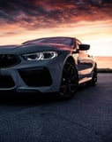 Front view of a BMW M8 with a vibrant sunset in the background, featured on a watch face