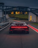 Rear view of a Bugatti Chiron with a red taillight on a racetrack during dusk, featured on a watch face.