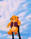 Illustration of baby Simba being held up against a bright blue sky, featured on a watch face.