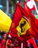 Close-up of Ferrari flags with the iconic prancing horse emblem, waving at an event, featured on a watch face.