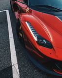 Close-up of the front view of a red Ferrari supercar, showcasing sleek lines and signature headlights, featured on a watch face.