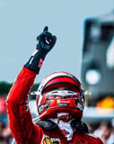 A Ferrari F1 driver in a red racing suit and helmet raising a gloved hand in celebration, featured on a watch face.