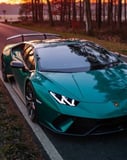 Teal Lamborghini Huracán parked on a forest-lined road at sunset, showcasing luxury and nature, featured on a watch face.