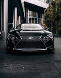 Front view of a black Lexus car parked in an urban setting, featured on a watch face.