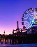 The Ferris wheel at Santa Monica Pier lit up against a colorful sunset sky, designed for a watch face