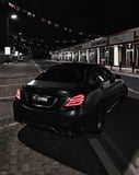 Rear view of a black Mercedes-Benz driving through a dark, city street at night, featured on a watch face.
