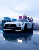 Mercedes-Benz AMG GT in white, parked on a reflective wet surface with an industrial backdrop, featured on a watch face.