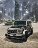 Mercedes-Benz G-Wagon parked in a cityscape at night, featuring glowing skyscrapers, on a luxury watch face.