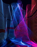Flowing neon light trails in blue and red creating wave-like patterns against a dark background, featured on a watch face.