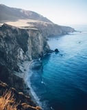 Scenic view of coastal cliffs overlooking deep blue ocean waters with a secluded sandy beach, designed for a watch face.