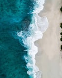 Aerial view of ocean waves washing onto a sandy beach with turquoise waters, designed for a watch face.