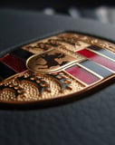 Close-up of the Porsche gold emblem with intricate details on a dark surface, featured on a watch face.