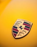 Close-up of the Porsche emblem on a vibrant yellow surface, featured on a watch face.