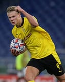 Image of Erling Haaland in a Borussia Dortmund jersey holding a football with a determined expression, featured on a watch face.