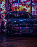 Photograph of a modified JDM sports car with racing decals parked under neon city lights in Japan, reflecting a cyberpunk aesthetic, featured on a watch face.
