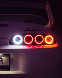 Close-up photograph of a white JDM Supra’s glowing circular taillights at night, showcasing its sleek design and street racing aesthetic, featured on a watch face.