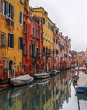 Photograph of a Venice canal lined with colorful historic buildings, with boats floating on the water and reflections creating a serene scene, featured on a watch face.