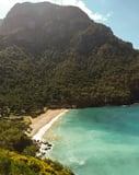 Photograph of a secluded tropical beach with golden sand, turquoise waters, and lush green mountains, creating a serene and picturesque scene, featured on a watch face.